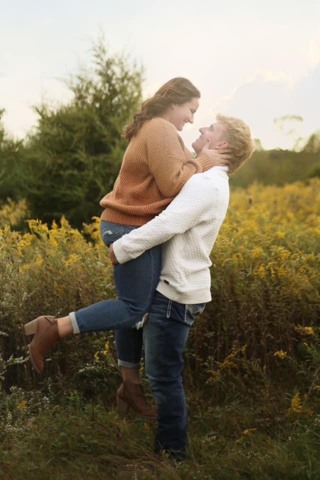couple in photo with man lifting women off the ground and women has foot lifted in air