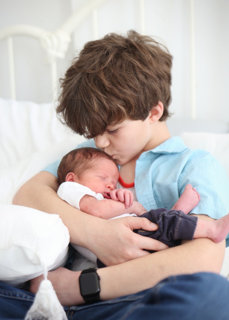 young boy holding newborn brother and kissing him on the forehead