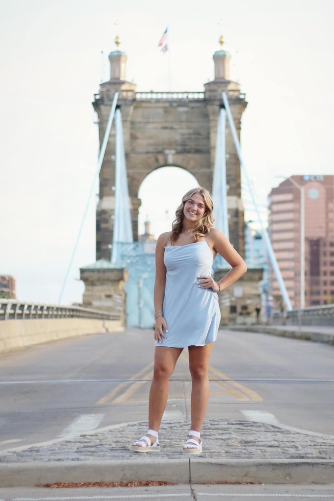 women standing in front of the bridge in Cincinnati wearing a blue dress and white sandals smiling